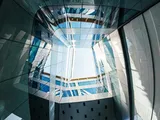 Looking up through a modern glass building interior, with a geometric skylight grid opening to bright sky above.
